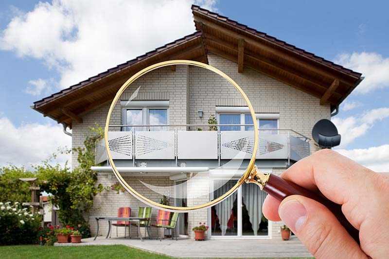 Hand holding a magnifying glass in front of a house while home inspection services are being preformed